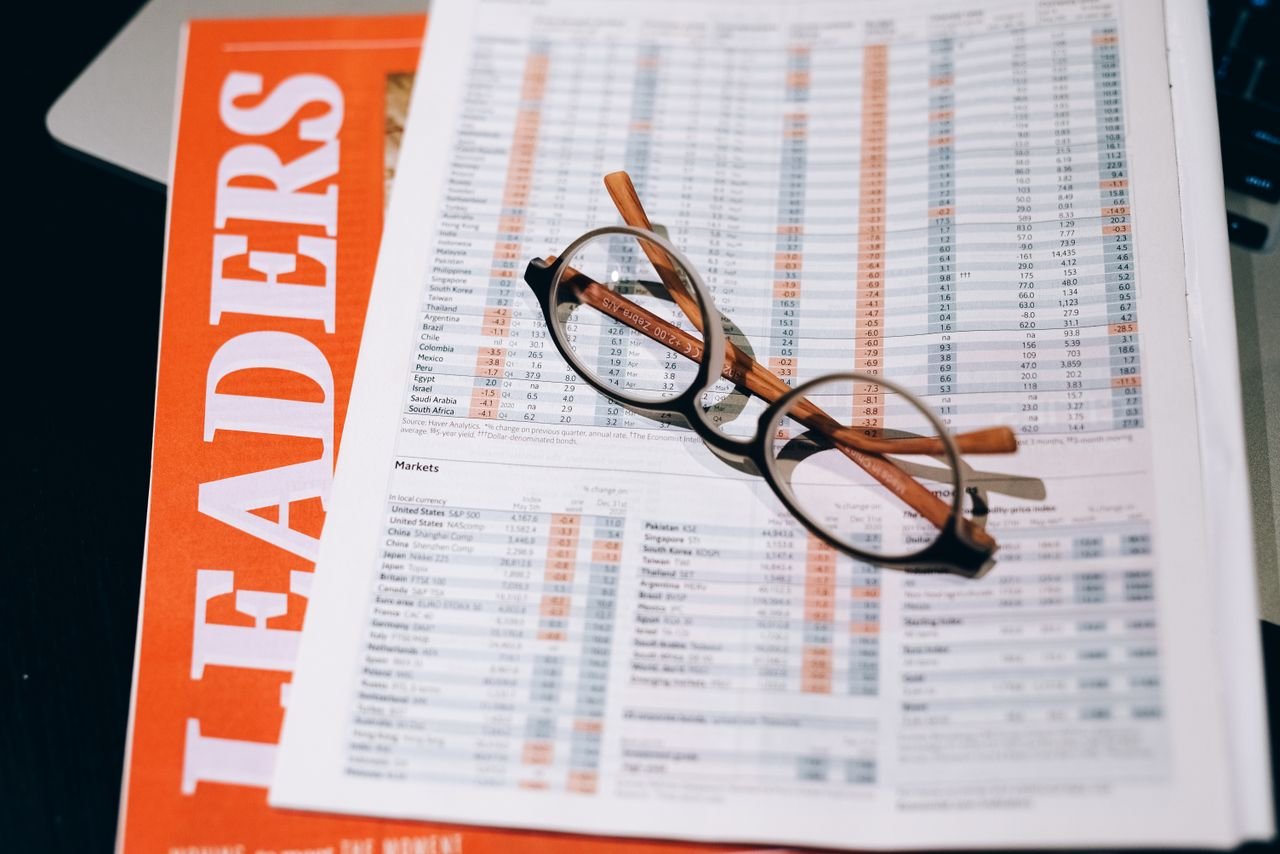 contact-img A pair of eyeglasses resting on a financial document and magazine with bold headline "LEADERS" in focus.